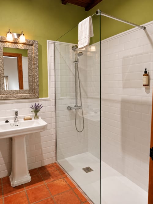 Baño moderno con azulejos blancos tipo metro, paredes verde lima, lavamanos de pedestal, ducha con mamparas de cristal y piso de terracota en El