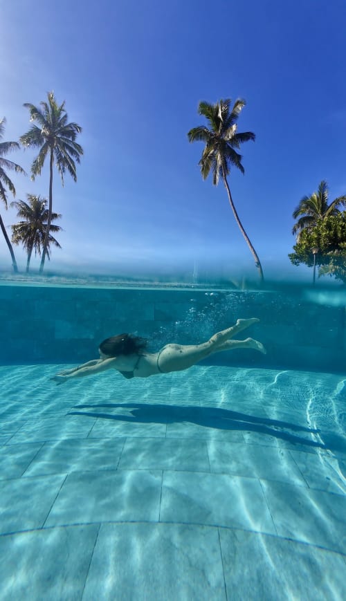 Woman snorkeling underwater at Sublime Tahiti Beach Retreat with palm trees and clear turquoise waters