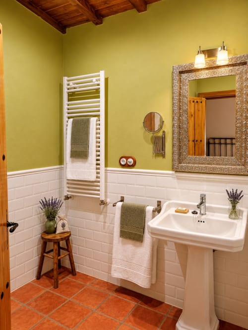Baño amarillo brillante con azulejos blancos tipo metro, lavamanos pedestal, toallero y espejo ornamentado en El descanso del peregrino