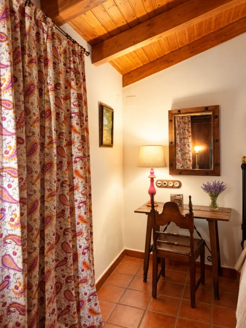 Acogedora habitación boutique con vigas de madera, cortinas florales, escritorio, lámpara y espejo en El descanso del peregrino en Guadalupe