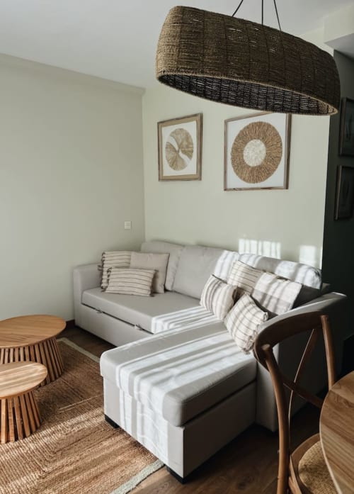 Acogedora habitación en Alojamientos Montaña Leonesa con sofá beige, cojines rayados, lámpara colgante tejida y cuadros decorativos.