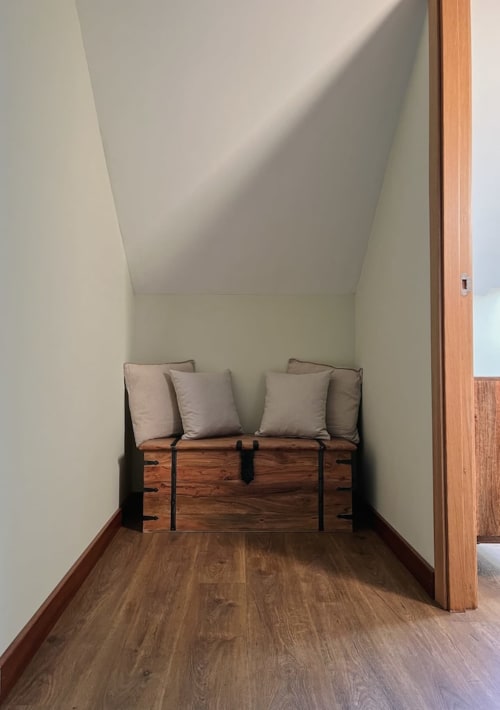 Acogedor rincón de dormitorio en Alojamientos Montaña Leonesa con baúl de madera, cojines grises y vistas a la montaña