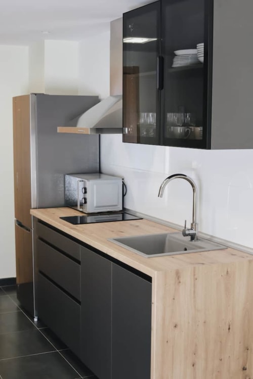 Pequeña cocina moderna con encimera de madera, muebles negros y fregadero de acero inoxidable en Alojamientos Montaña Leonesa