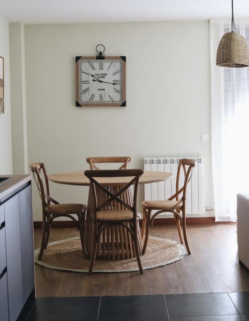 Comedor en El Mirador del Susarón con mesa redonda de madera, sillas thonet y reloj vintage en Alojamientos Montaña
