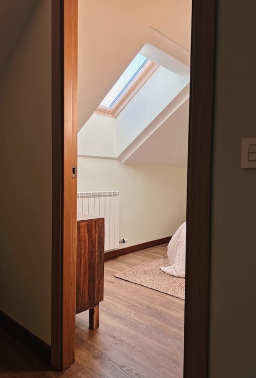 Luminoso dormitorio en ático con tragaluz, vigas de madera, radiador y suelos de parquet en Alojamientos Montaña Leonesa