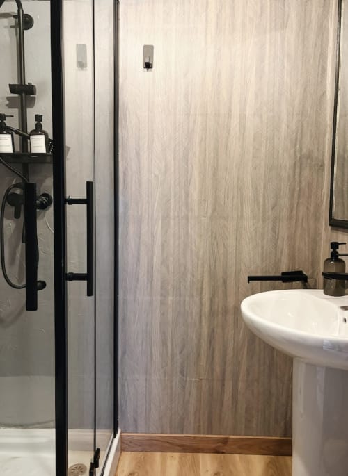 Baño moderno en La Casina de Isoba con ducha abierta, azulejos veteados, lavabo pedestal y accesorios negros