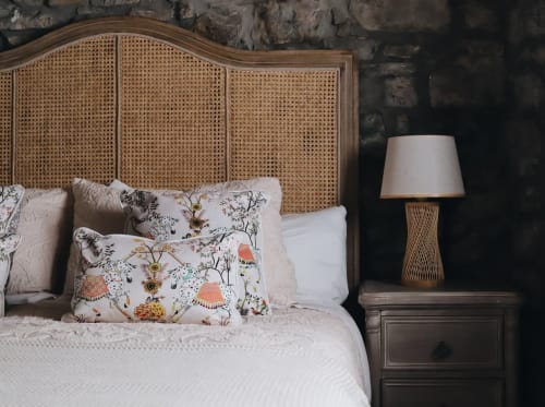 Cama con cabecero de ratán y almohadas florales en Alojamientos Montaña Leonesa, habitación La Casina de Isoba con vistas al jardín