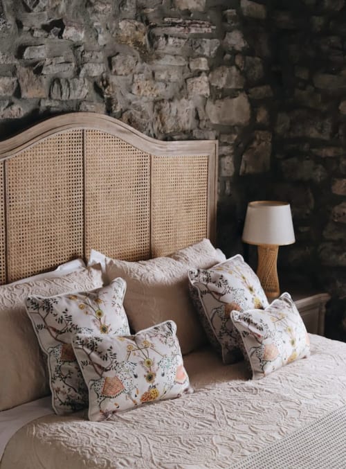 Dormitorio rústico en Alojamientos Montaña Leonesa con cabecero de ratán, almohadas florales y pared de piedra