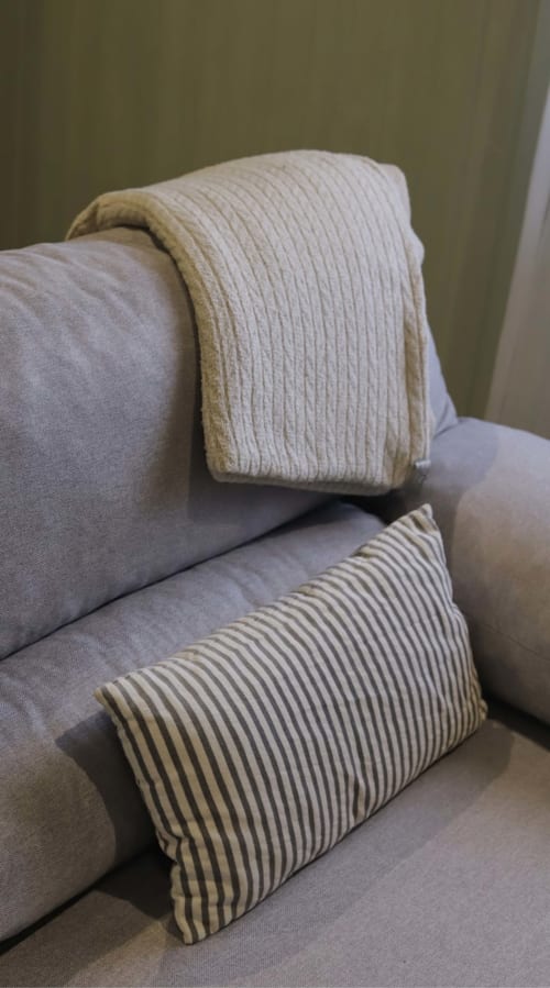 Cojines beige y manta sobre silla tapizada gris en la habitación de huéspedes de La Casina de Isoba