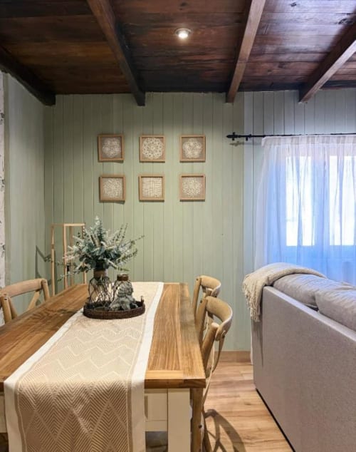 Acogedora habitación de refugio de montaña con mesa de comedor, vigas de madera, paredes color salvia y cuadros en Alojamientos Montaña Leonesa