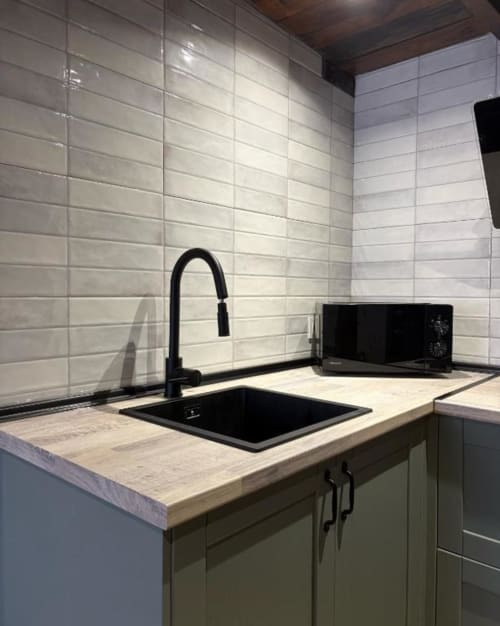 Cocina moderna con fregadero negro, grifo elegante, azulejos blancos tipo metro y encimera de madera clara en Alojamientos Montaña