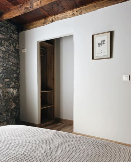 Dormitorio moderno con vigas de madera vista, pared de piedra, paredes blancas y armario abierto en Alojamientos Montaña Leonesa