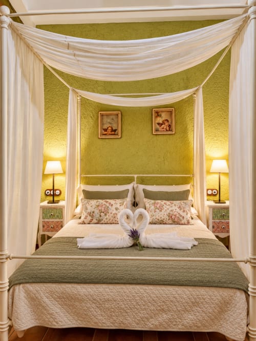 Cama con dosel de lujo y cortinas color crema en habitación boutique de El descanso del peregrino, Guadalupe. Paredes amarillas, ambiente acogedor.