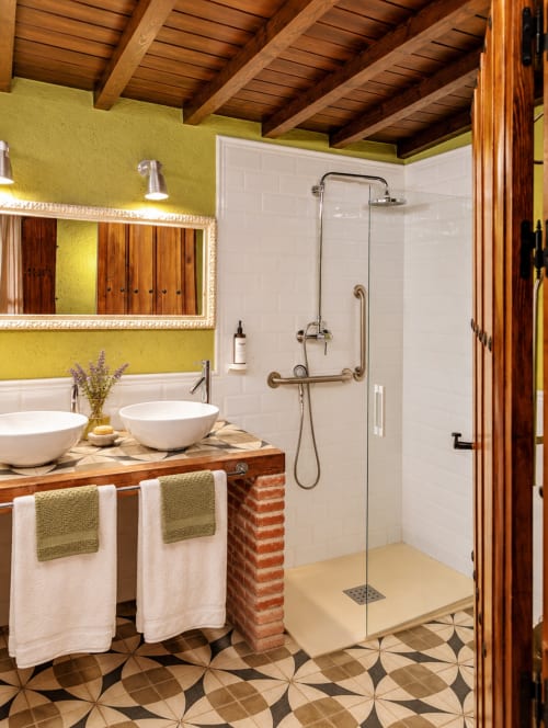 Baño boutique en El descanso del peregrino de Guadalupe con paredes amarillo lima, vigas de madera, lavabos tipo vessel y ducha a ras de suelo