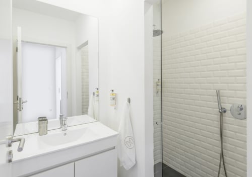 Banheiro moderno no apartamento Oporto Comfort Dom Hugo Porto com pia branca, espelho grande e boxe azulejado