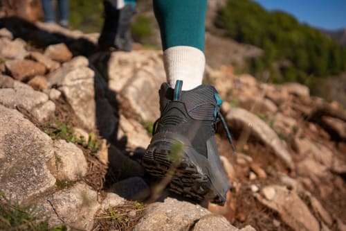 Escursionista in leggings teal e stivali neri su sentiero di montagna rocciosa vicino ad Antico Belvedere, Italia