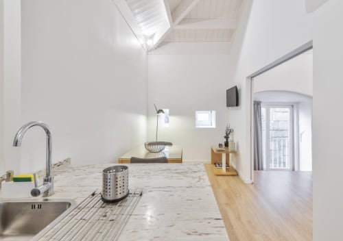 Modern kitchen and living area in Porto apartment with marble countertop, stainless steel sink, wooden flooring, and skylight