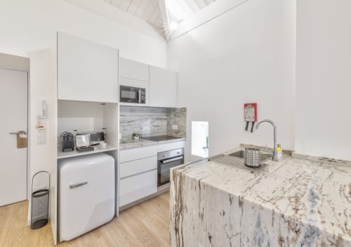 Modern kitchenette with white cabinets, marble countertop, and appliances in Porto apartment