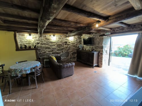 Sala de estar de apartamento de piedra rústica con vigas de madera vista, sillón de cuero marrón y acceso al jardín exterior en Bikarte