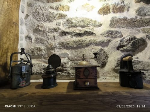 Lámparas de aceite antiguas y artículos de cocina vintage exhibidos contra muro de piedra rústica en Bikarte Alojamientos en Ribeira Sacra