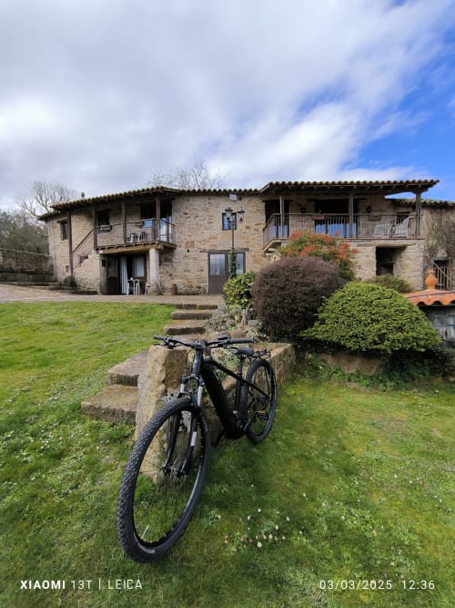 Bicicleta eléctrica negra estacionada en el jardín de Bikarte Alojamientos, propiedad rural de piedra en Ribeira Sacra