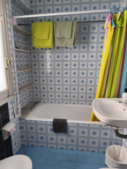Baño de la Pensión Los Pinos Gijón con azulejos azules decorativos, bañera, lavabo y toallas de colores en el toallero