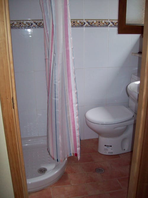 Baño de la Pensión Los Pinos Gijón con ducha, inodoro y azulejos blancos