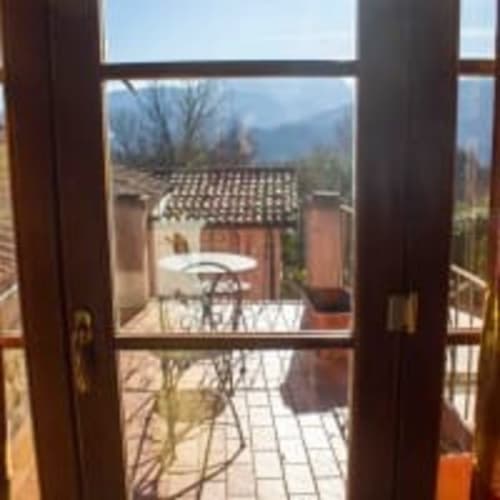 Vista dalla camera Belvedere Sopra dell'Antico Belvedere B&B attraverso le porte in legno sul giardino e gli edifici in terracotta con montagne