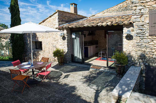 Terrasse de la Suite Bleuet au Clos des Amandiers, Simiane-la-Rotonde, avec bâtisses en pierre, parasol et mobilier de jardin