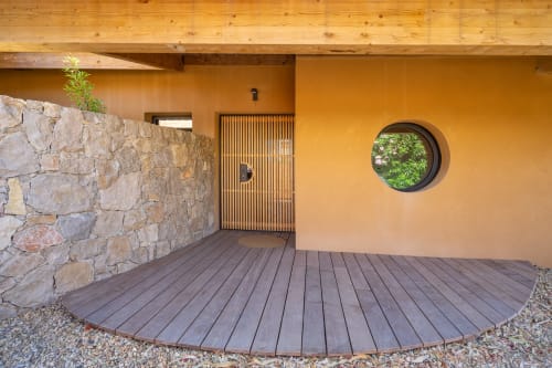 Entrée élégante de la villa moderne au Lord Resort avec murs en terre cuite, terrasse en bois, éléments en pierre et fenêtre circulaire offrant une vue panoramique