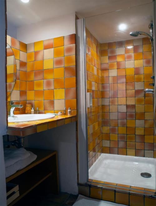 Salle de bain moderne avec carrelage orange vibrant, lavabo blanc et douche ouverte au Clos des Amandiers