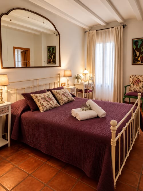 Elegante dormitorio de villa en El descanso del peregrino con ropa de cama burdeos, cama de metal crema, espejo y vistas a la montaña
