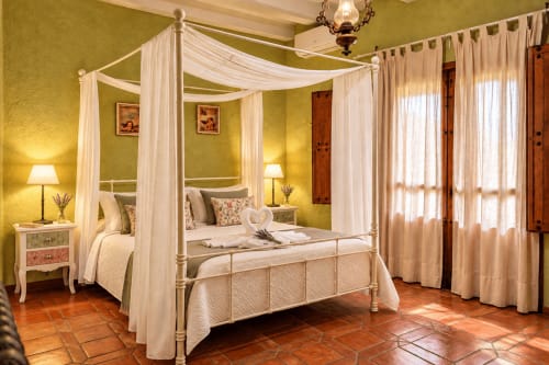 Cama con dosel elegante y cortinas blancas en la suite verde de El descanso del peregrino, Guadalupe, España
