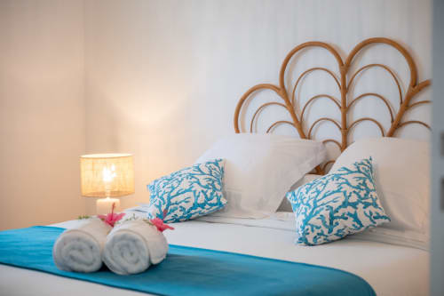 Coastal bedroom at Vista Del Mar with blue coral pillows, woven headboard, rolled towels, and bedside lamp in Guadeloupe