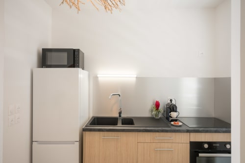 Modern kitchenette at Vista Del Mar Sainte-Anne with black countertop, wood cabinets, microwave, and stainless steel sink