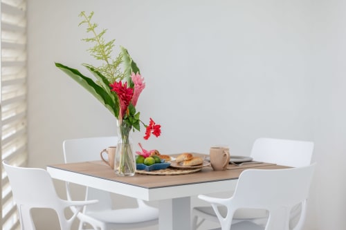 Modern dining table at Vista Del Mar Guadeloupe with fresh flowers, fruit, pastries, and white chairs in bright apartment