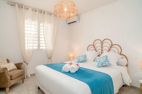 Bright bedroom at Vista Del Mar, Guadeloupe with white bed, blue accent pillows, woven headboard, and tropical decor