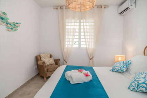 Bright bedroom at Vista Del Mar Guadeloupe with blue runner, rolled towels with flowers, beige curtains, and tan armchair