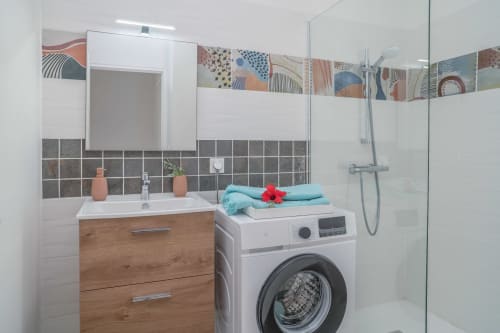 Modern bathroom with wooden vanity, washing machine, teal towels, and decorative tile accents at Vista Del Mar, Guadeloupe