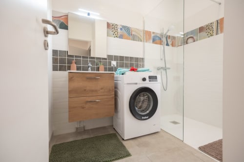 Modern bathroom at Vista Del Mar apartment in Guadeloupe with washing machine, wooden vanity, black tile accents, and walk-in