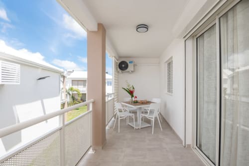 Modern apartment balcony at Vista Del Mar with white dining table, potted flowers, and sea views in Sainte-Anne, Guadeloupe