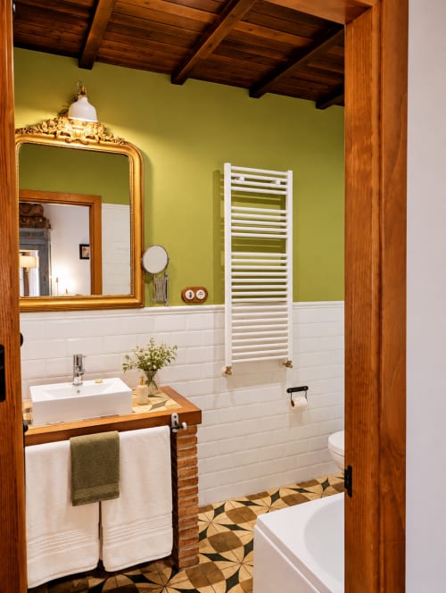 Elegante baño con azulejos verde lima y blanco, vigas de madera, espejo con marco dorado y piso geométrico en El Descanso del