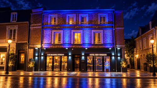 Hôtel New Windsor Etretat la nuit : façade illuminée en bleu, café au rez-de-chaussée, plaza mouillée et ciel étoilé
