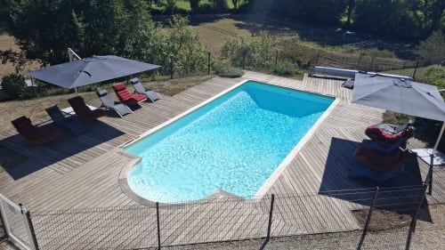 Piscine rectangulaire aux eaux bleues, terrasse en bois, transats, parasols et clôture de sécurité aux Gîtes Le Pech