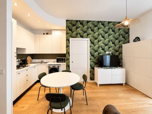 Monolocale moderno alle Seven Suites Sanremo con cucina bianca, tavolo da pranzo, mobile TV e parete decorativa con motivi di felci