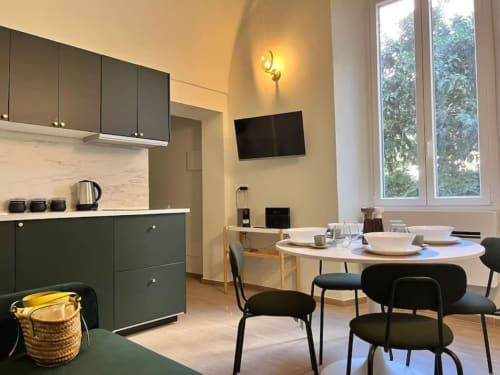 Moderna cucina-sala da pranzo di Seven Suites Sanremo con mobili verde scuro, tavolo rotondo e vista sul giardino