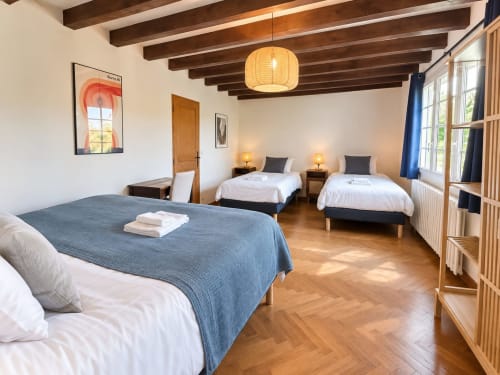 Chambre spacieuse du gîte Maison Héléna à Lain avec trois lits, poutres apparentes et lumière naturelle par les fenêtres