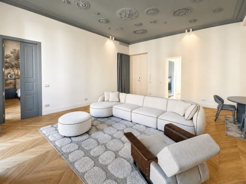 Soggiorno moderno alle Seven Suites Sanremo con divano componibile curvo, pouf e pavimento in legno a spina di pesce