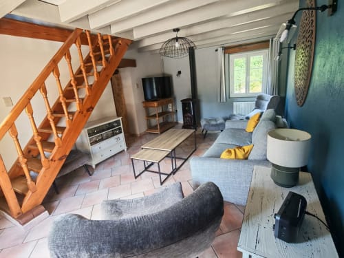 Séjour de la Maison du Pech avec escalier en bois, canapé gris, TV et vue sur le jardin aux Gîtes Le Pech