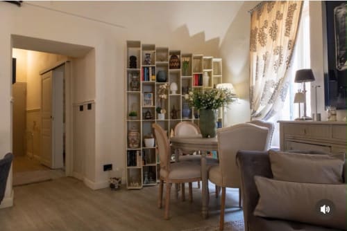 Elegante zona living ai Seven Suites Sanremo con arredi moderni, scaffalature integrate e luce naturale dalle finestre drappe